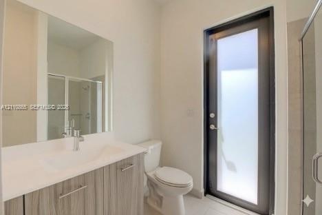 Bathroom featuring a vanity with a light wood-finish cabinet and solid surface countertop, an oversized wall-mounted mirror, a full-height glass-panel