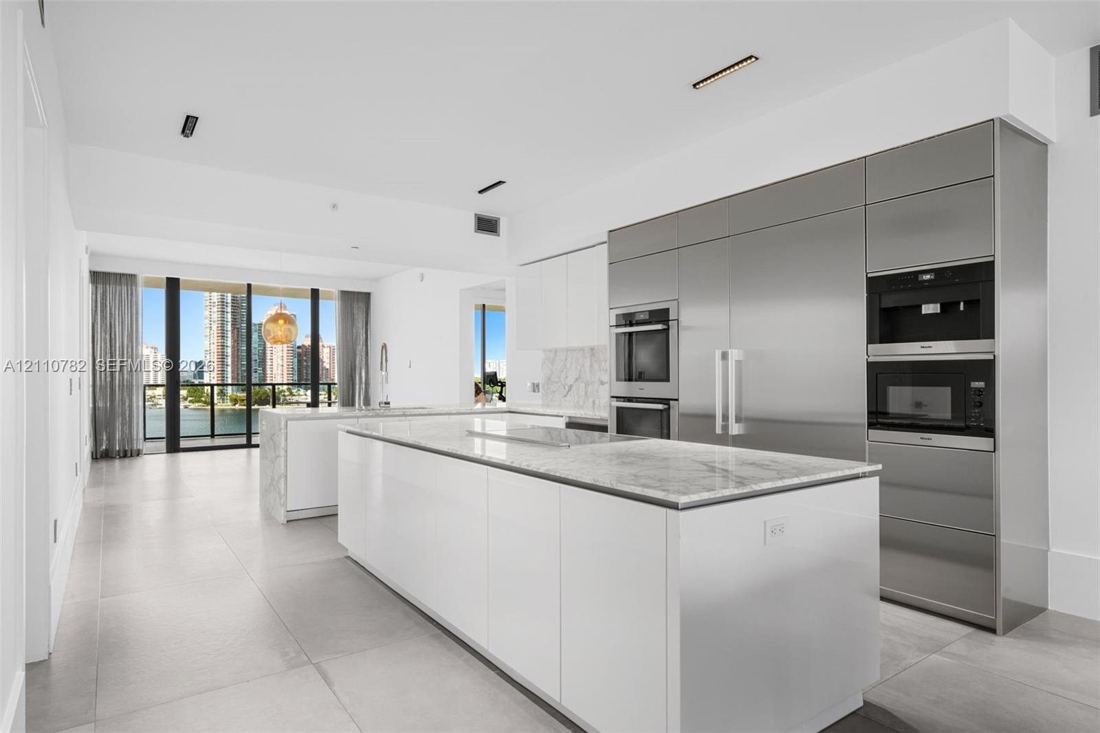 Contemporary kitchen featuring dual islands with stone-surface countertops, floor-to-ceiling cabinetry, integrated stainless steel appliances, and lar