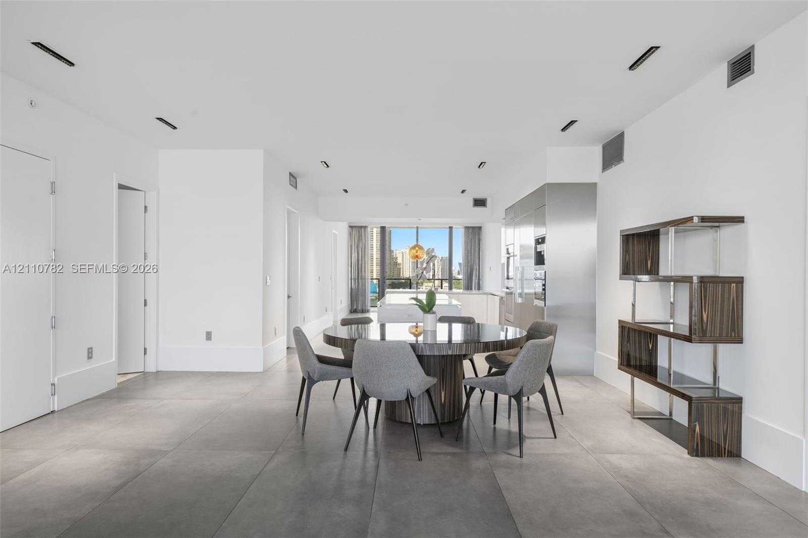 Open-concept space featuring large-format ceramic tile flooring, floor-to-ceiling windows, integrated stainless steel kitchen cabinetry, and recessed 