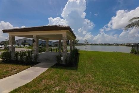 Covered pavilion featuring stone-clad pillars, concrete flooring, and a tiled roof, set against a waterfront backdrop