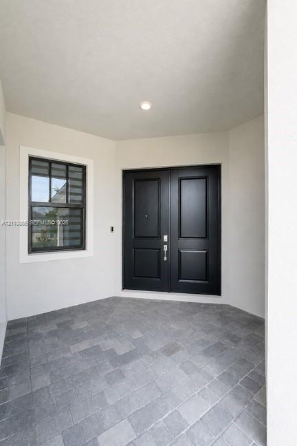 Covered entryway featuring double doors with matte black finish, stone-paver flooring, and a multi-pane window with dark trim
