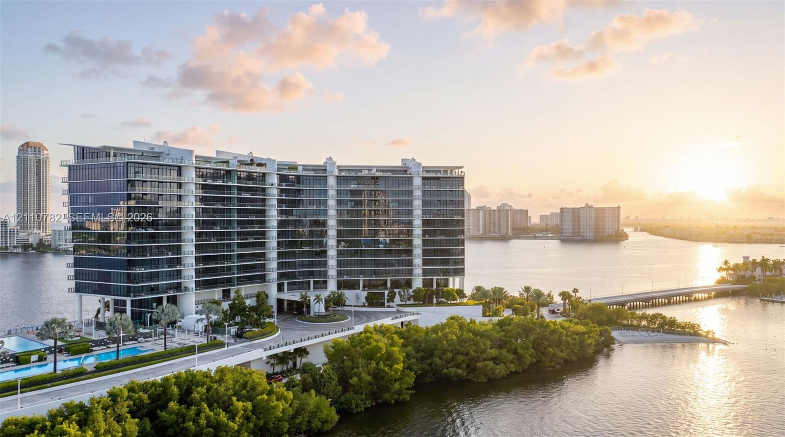 High-rise residential building featuring floor-to-ceiling glass paneling, wrap-around balconies, a porte-cochère entryway, and an outdoor swimming poo