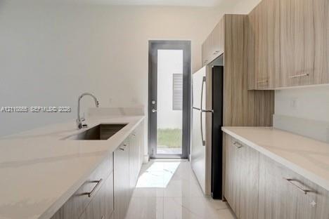 Kitchen featuring flat-panel wood-finish cabinetry, light-toned stone-finish countertops, stainless steel undermount sink with gooseneck faucet, full-