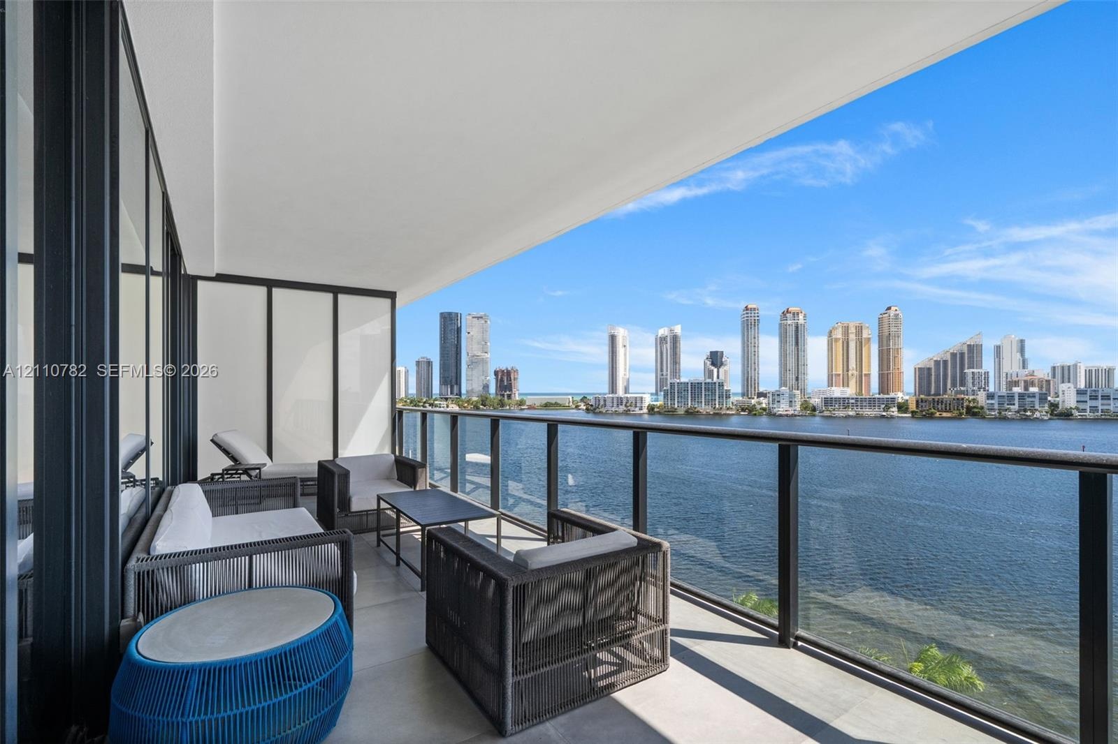 Covered balcony featuring tile flooring, glass-paneled railings with dark metal framing, and wide-reaching water and cityscape exposure