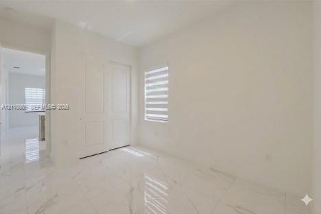 Neutral-toned interior featuring large-format tile flooring with a veined pattern, two-panel interior doors, and a window fitted with horizontal dual-