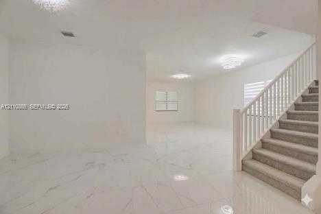 Open-concept interior featuring large-format polished tile flooring, a staircase with white balusters and neutral carpeting, multi-tier crystalline ch