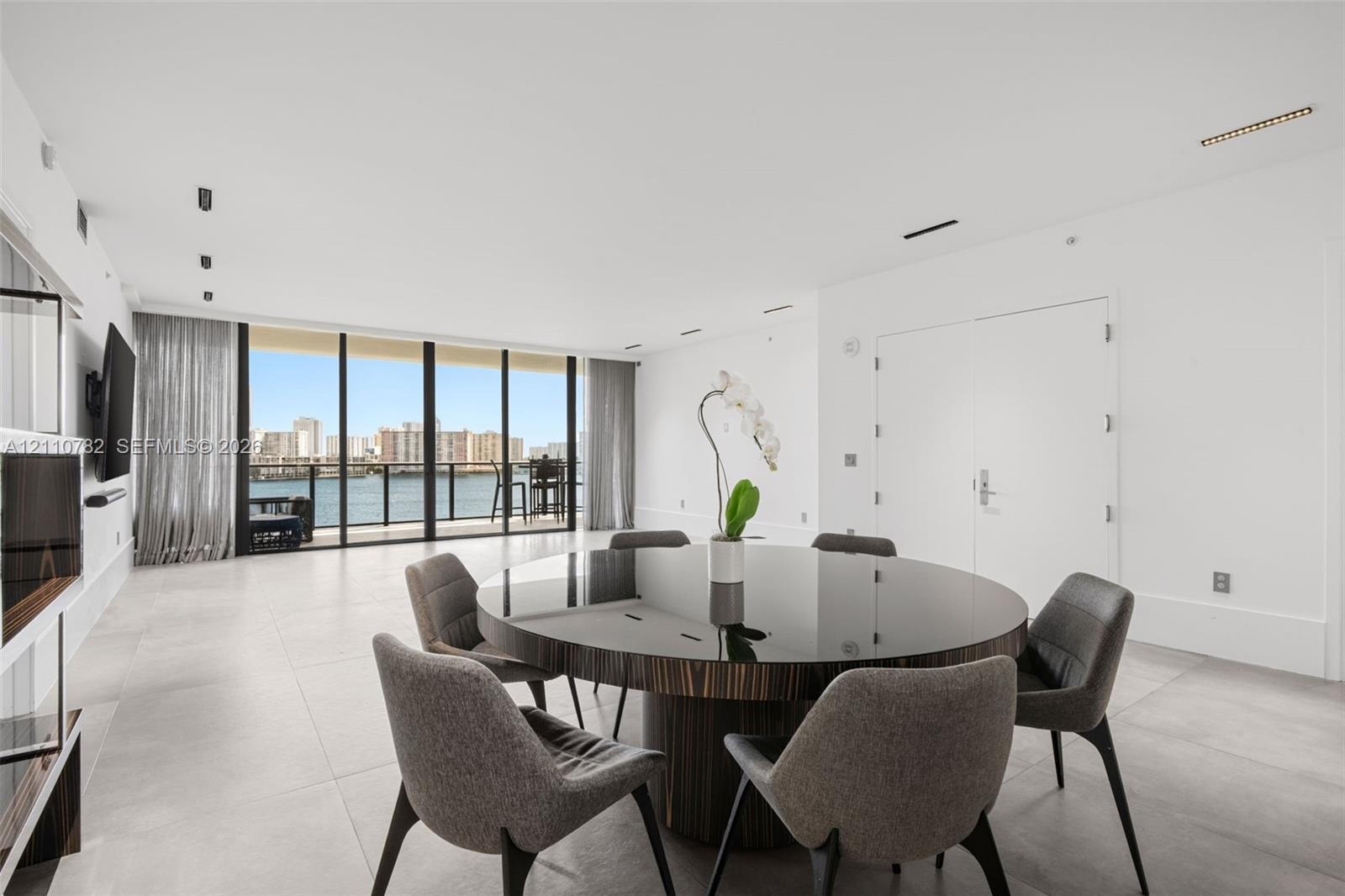 Open-concept interior featuring large-format tile flooring, floor-to-ceiling glass panel windows, integrated recessed lighting, and a private balcony