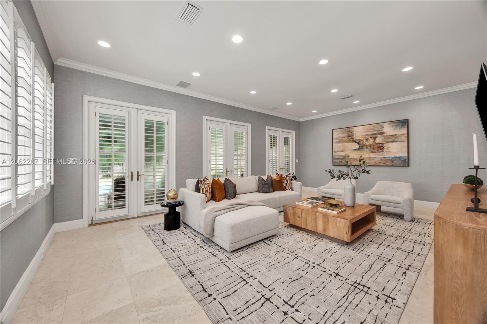 Neutral-toned interior space featuring light-colored stone flooring, recessed ceiling lighting, crown molding, and dual glass-paned French doors with 