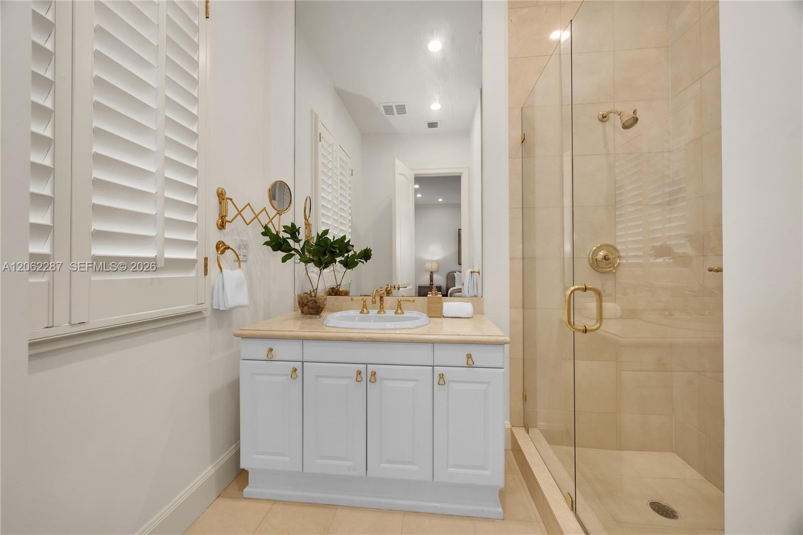 Bathroom featuring white cabinetry, stone-surface countertop, undermount sink, brass-finish fixtures, and a glass-enclosed shower with floor-to-ceilin