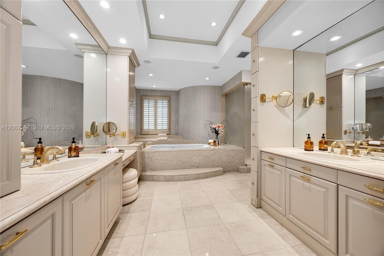 Dual vanities with recessed-panel cabinetry, stone countertops, integrated basins, recessed lighting, and a raised platform soaking tub