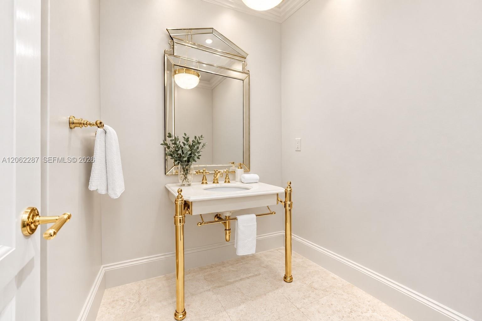 Console-style sink with stone countertop, polished gold-tone metal legs, decorative framed mirror, and coordinating gold-tone faucet and hardware