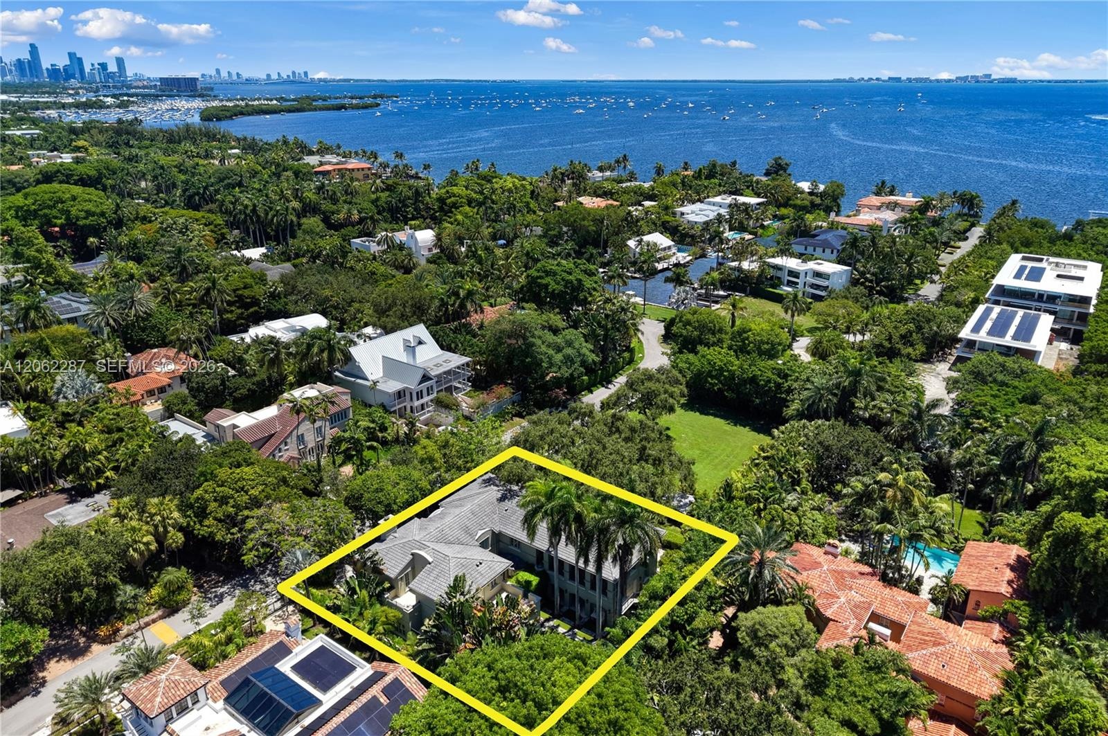 Aerial perspective of a multi-structure residence featuring a pitched roof, mature palms, dense landscaping, and expansive green space within the prop
