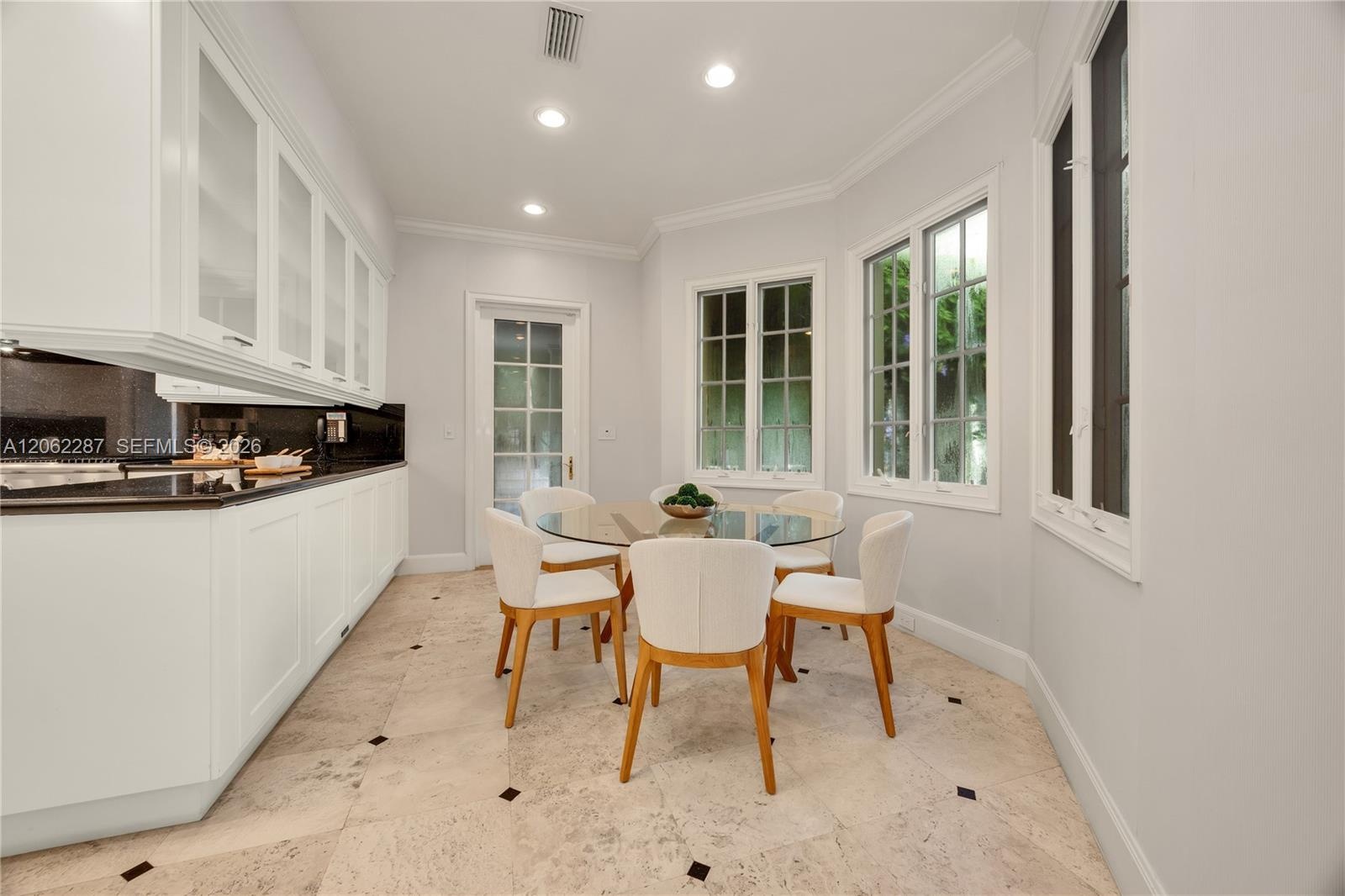 Custom white cabinetry with glass-panel upper doors, dark stone countertops, recessed lighting, multi-pane windows, and tile flooring with decorative 