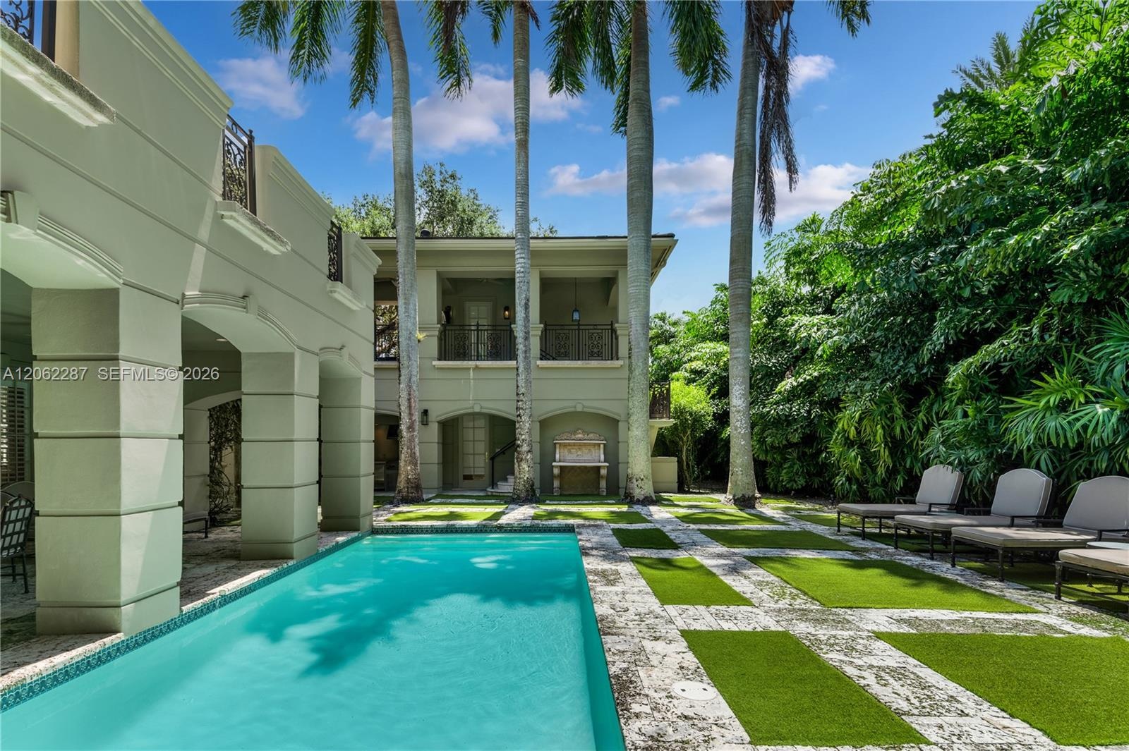 Stucco exterior featuring arched architectural detailing, two-story covered loggias with wrought-iron railings, stone-tiled pool deck, and a rectangul