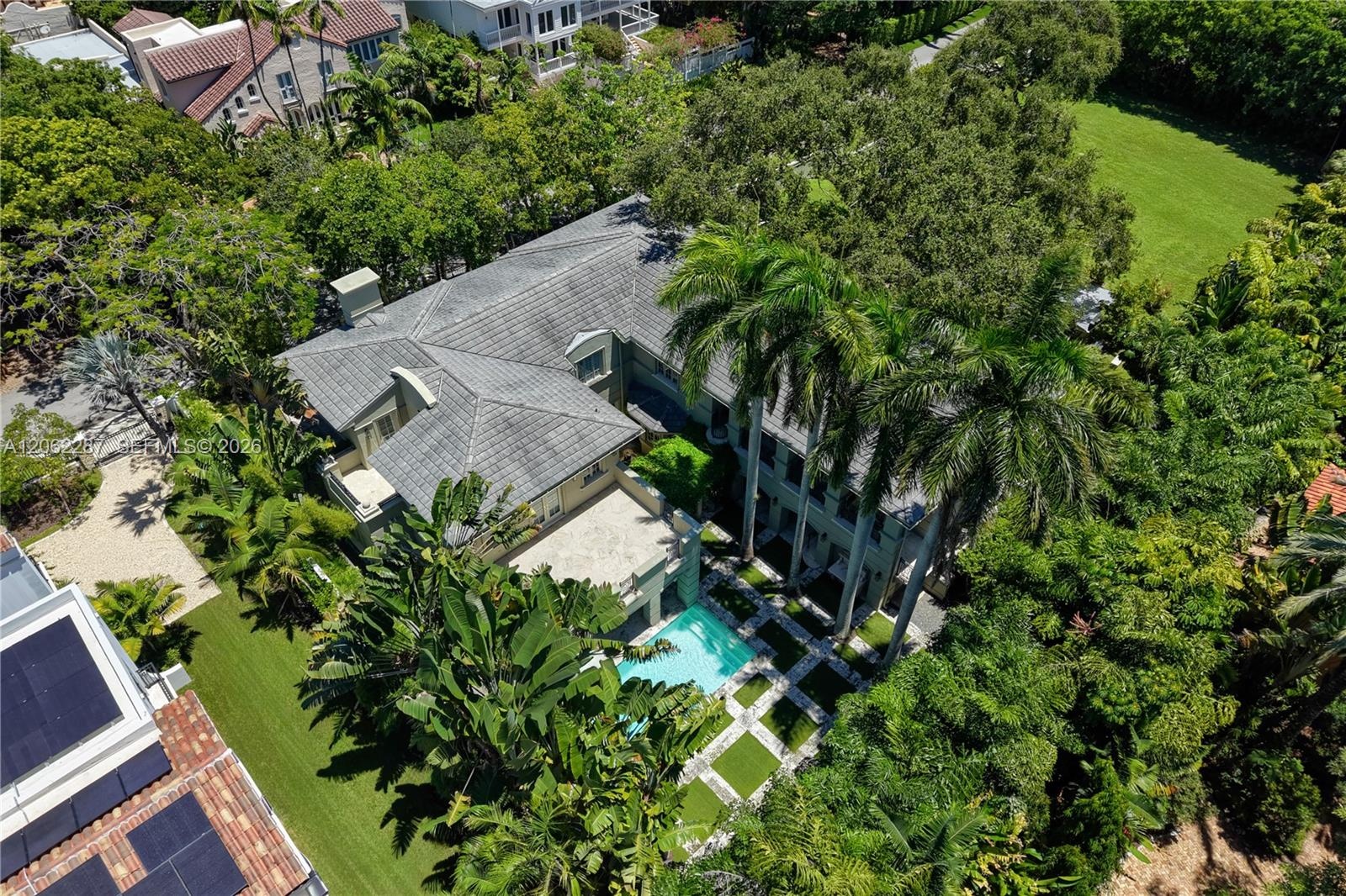 Aerial perspective of a multi-level estate featuring a tile roof, an in-ground swimming pool, stone-paver hardscaping, mature landscaping, and an expa