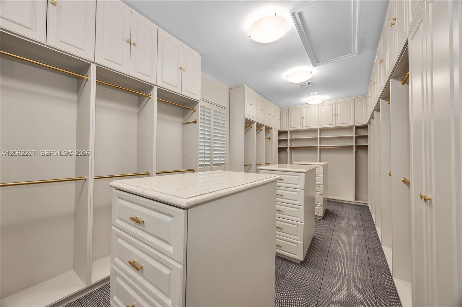 Custom built-in cabinetry featuring white shaker-style doors, dual islands with stone-composite countertops, matte gold hardware, tiered shelving, and
