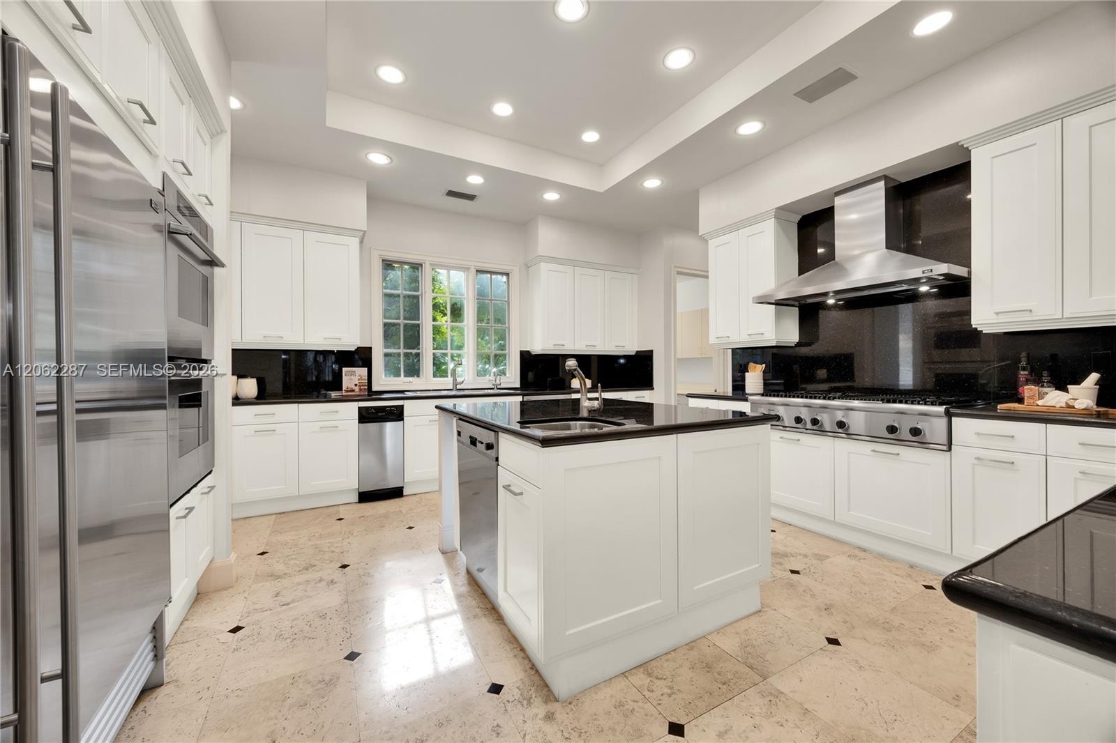 Kitchen featuring white shaker-style cabinetry, a central island with a stone countertop, stainless steel appliances, a professional-grade range hood,