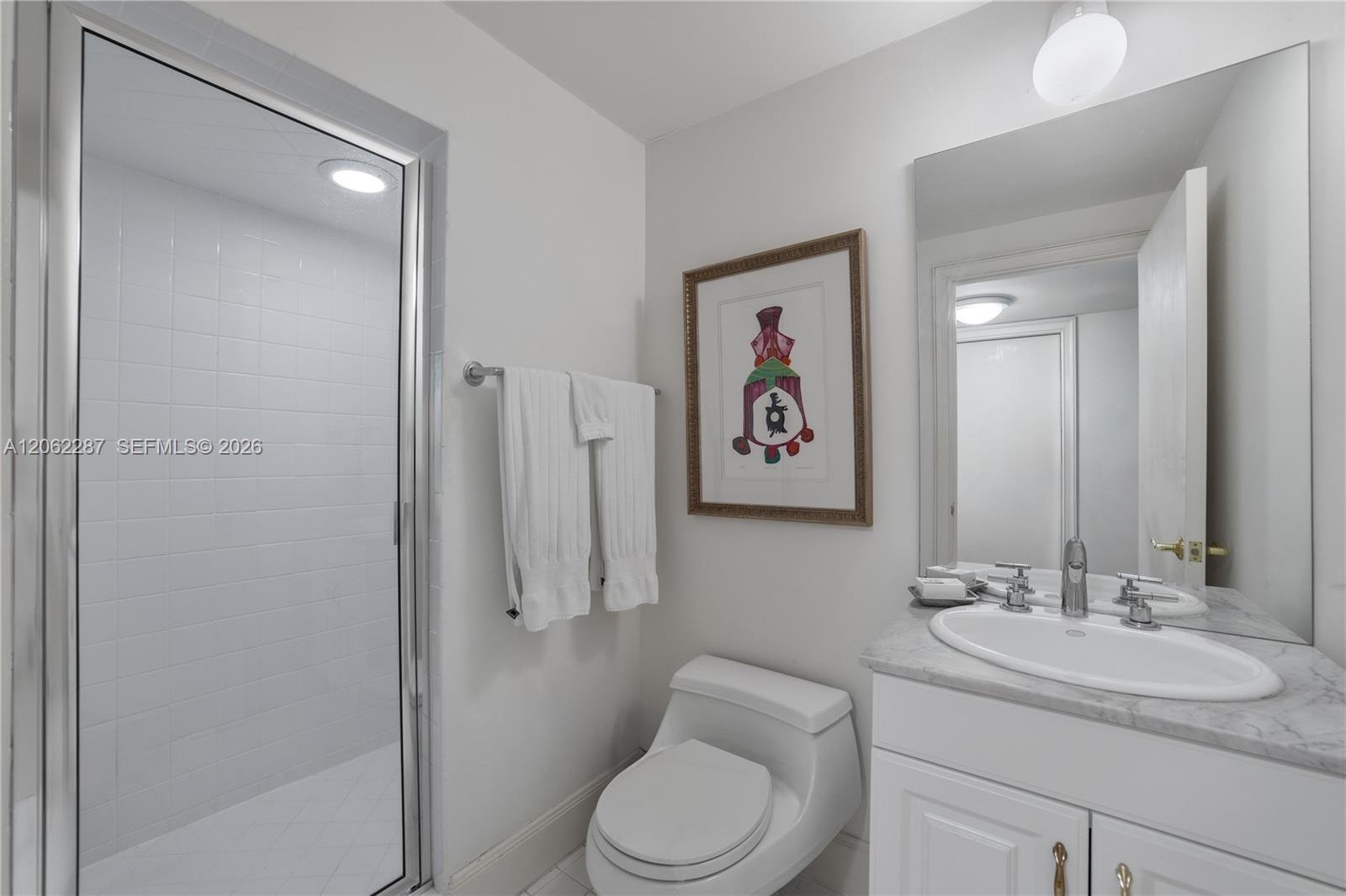 Staff Suite: Bathroom featuring a stone-top vanity with an integrated oval sink, chrome widespread faucet, frameless glass-enclosed shower with white 
