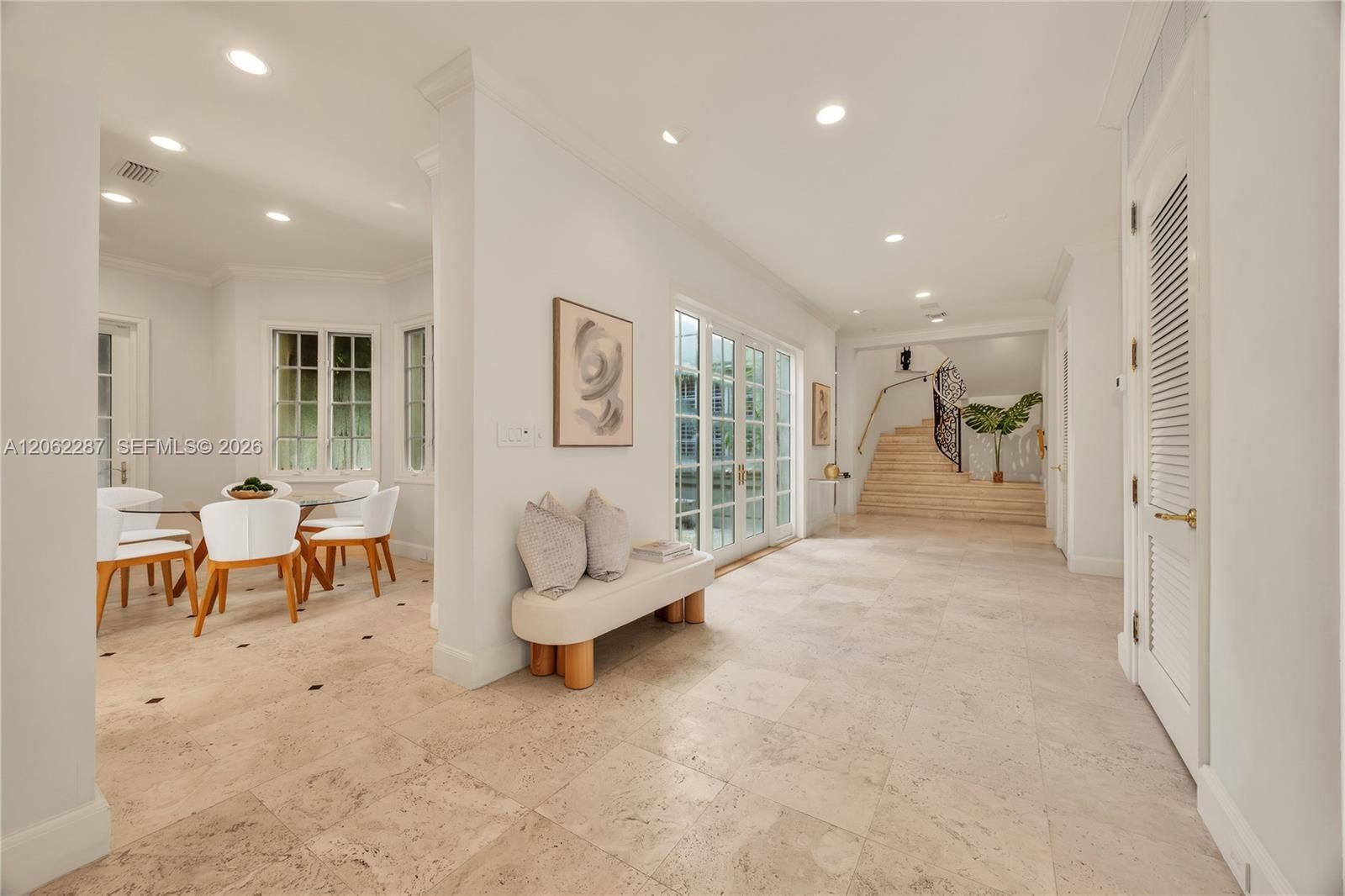 Open interior featuring large-format stone tile flooring, recessed lighting, double-paned glass French doors, and a staircase with a wrought-iron rail