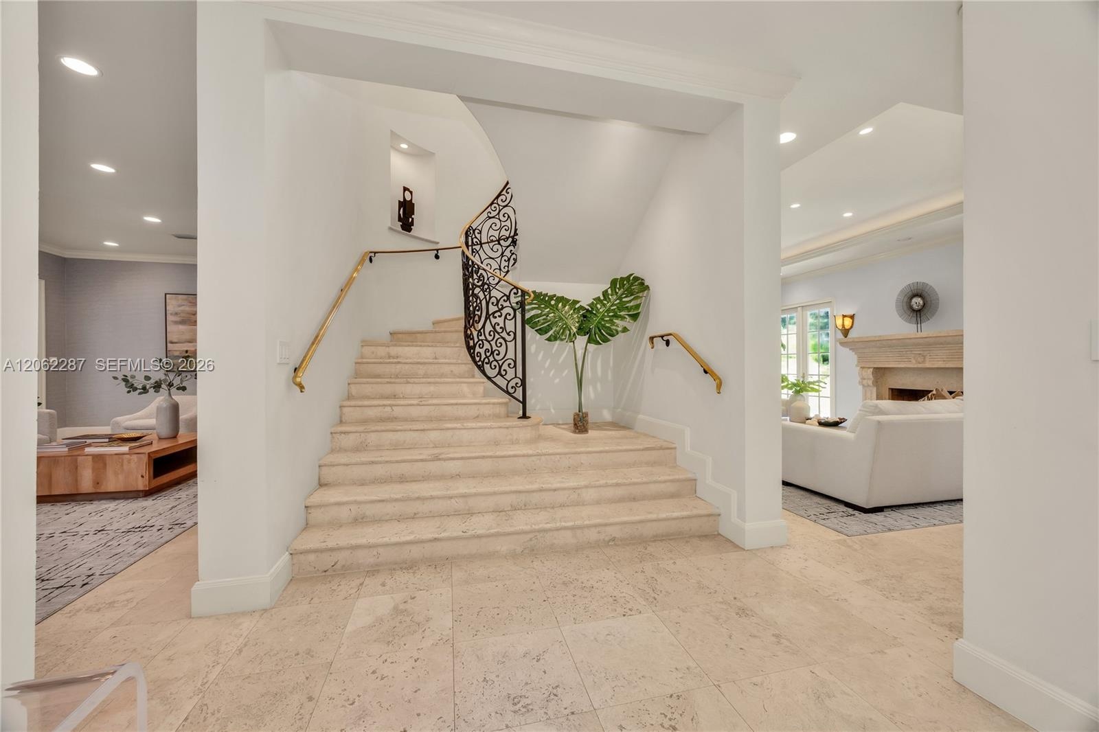 Grand foyer featuring a stone staircase with ornate iron railing, brass handrails, recessed wall niche, and natural stone flooring with recessed light