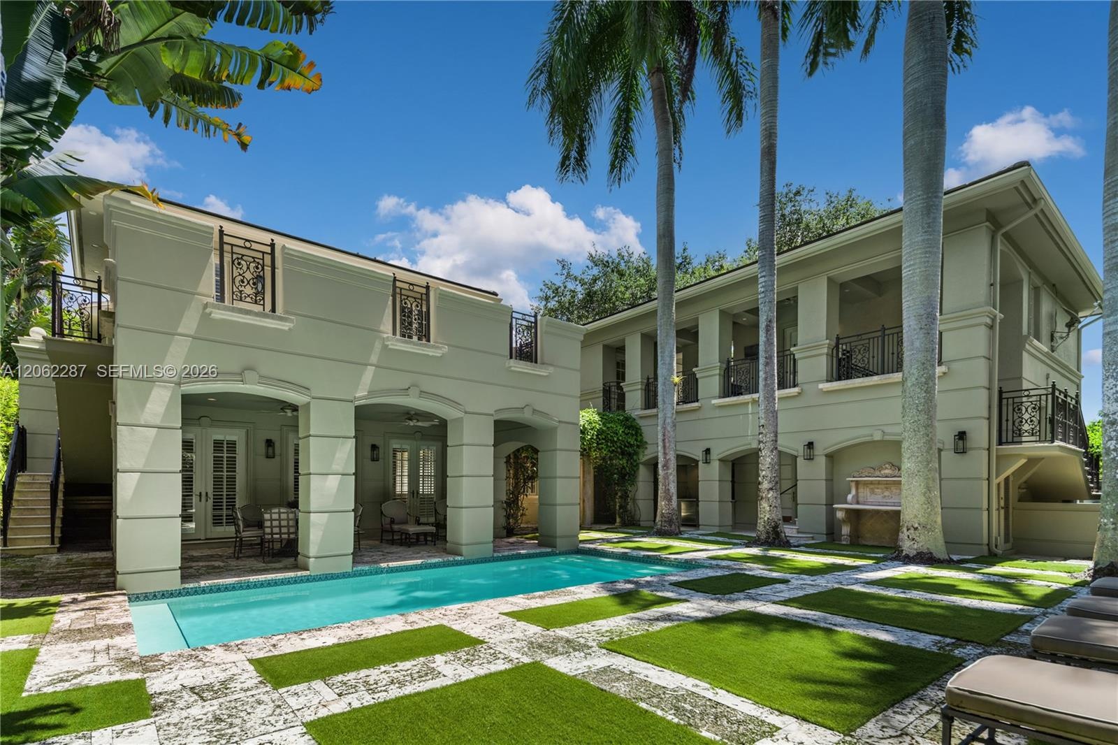 Two-story residence featuring a rectangular swimming pool, integrated covered loggias, ornamental iron balcony railings, stone-paver decking with turf