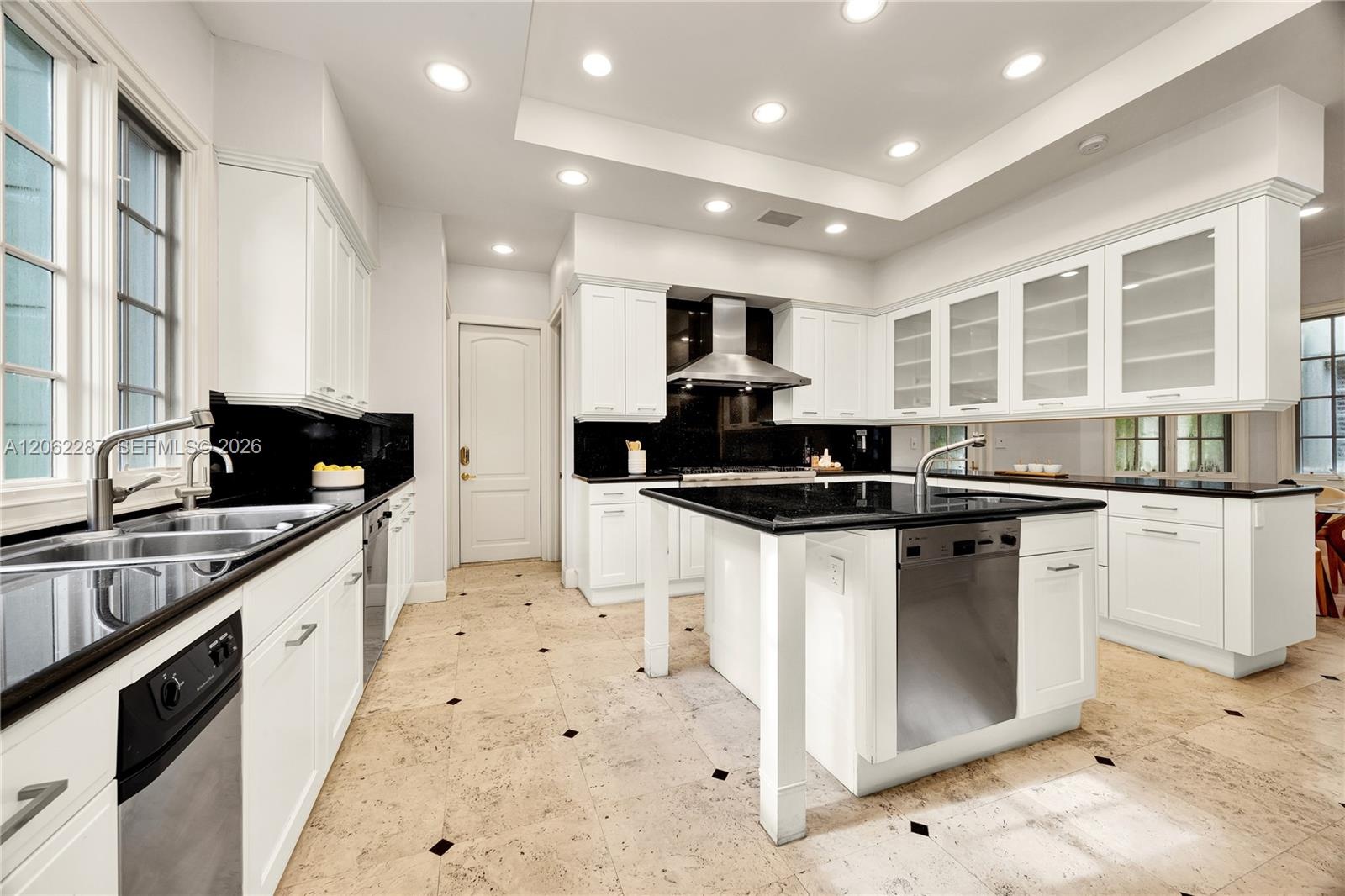 Kitchen featuring white shaker-style cabinetry, contrasting black countertops, a central island with integrated stainless steel dishwasher, recessed c