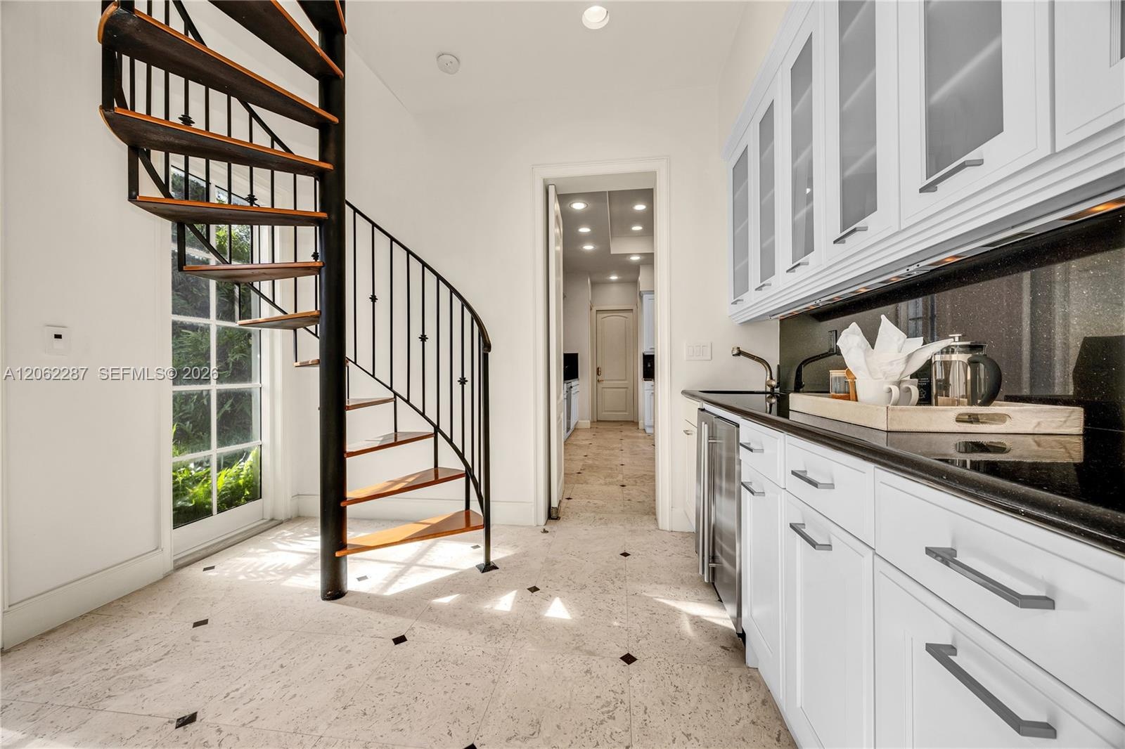 Spiral staircase with metal railing and wood-finish treads, custom white cabinetry featuring glass-front upper doors, dark stone-finish countertops, s