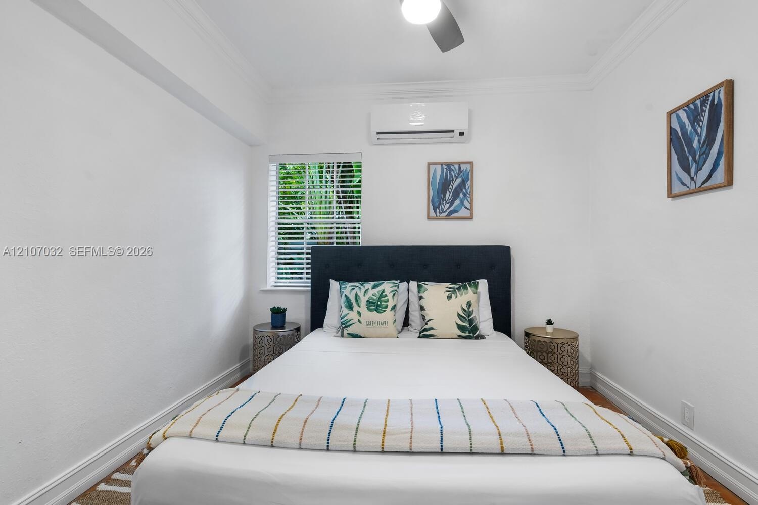 Neutral-toned room featuring wood-finish flooring, crown molding, a wall-mounted mini-split HVAC unit, and a single-pane window with horizontal blinds