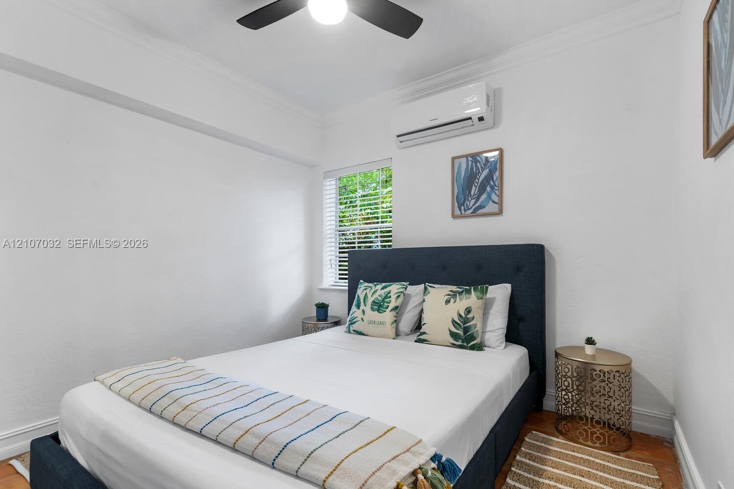 Interior space featuring wood-finish flooring, a wall-mounted ductless air conditioning unit, a multi-blade ceiling fan, and a window with white blind