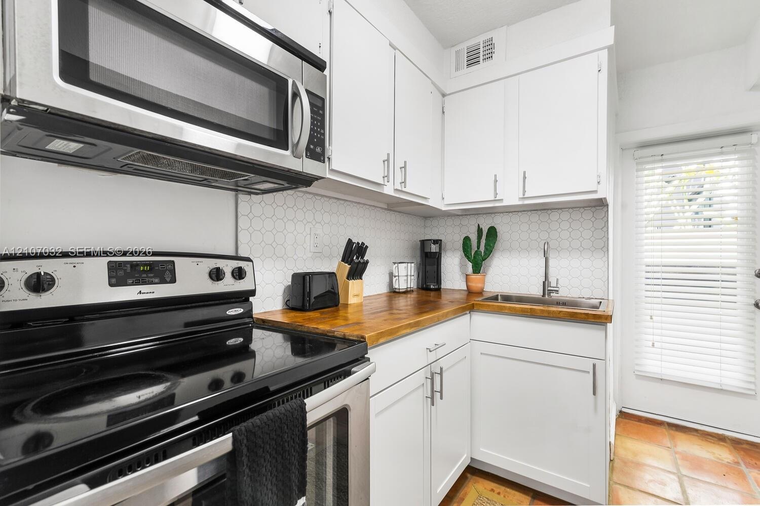 Kitchen featuring white cabinetry with metallic hardware, wood-finish countertops, stainless steel appliances, a hexagonal tile backsplash, and cerami