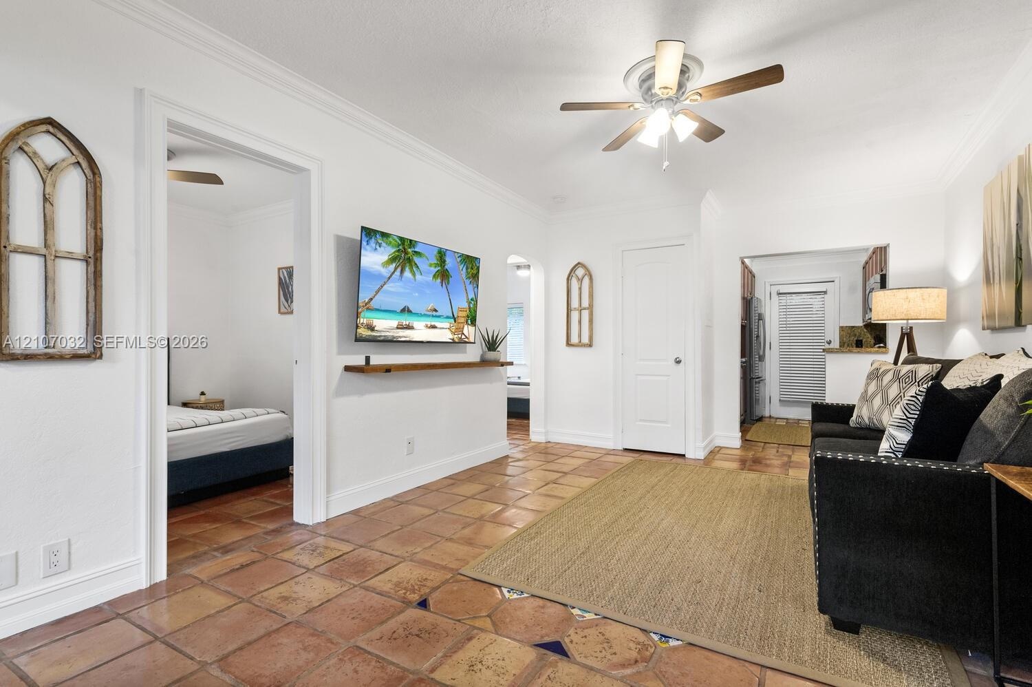Interior space featuring terracotta tile flooring, crown molding, a ceiling fan with integrated lighting, and a wall-mounted wooden shelf