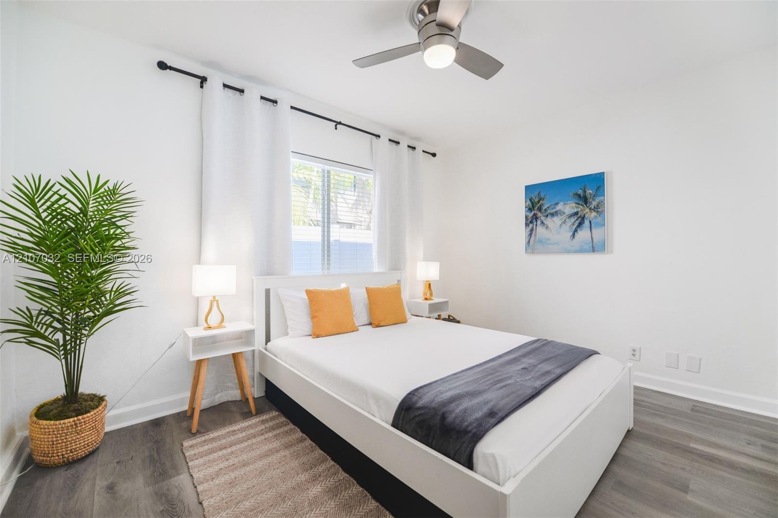 Neutral-toned bedroom featuring wood-finish flooring, a brushed metal ceiling fan with integrated lighting, and a single window framed by an adjustabl