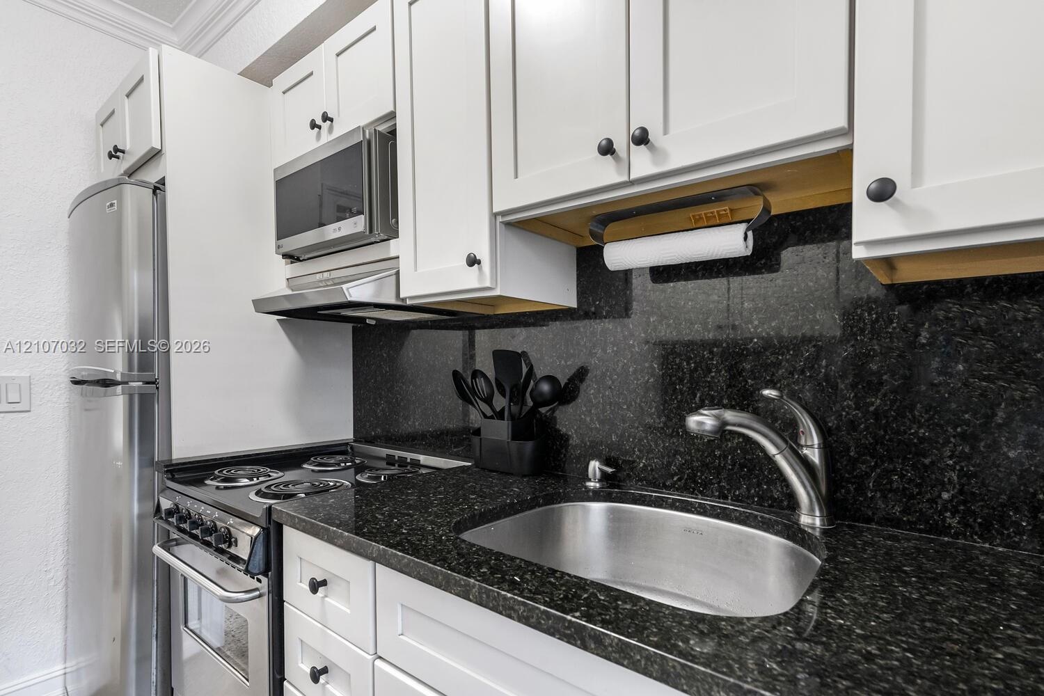 Kitchen featuring white shaker-style cabinetry, stone countertops, stainless steel appliances, and a deep-basin stainless steel sink with a high-arch 