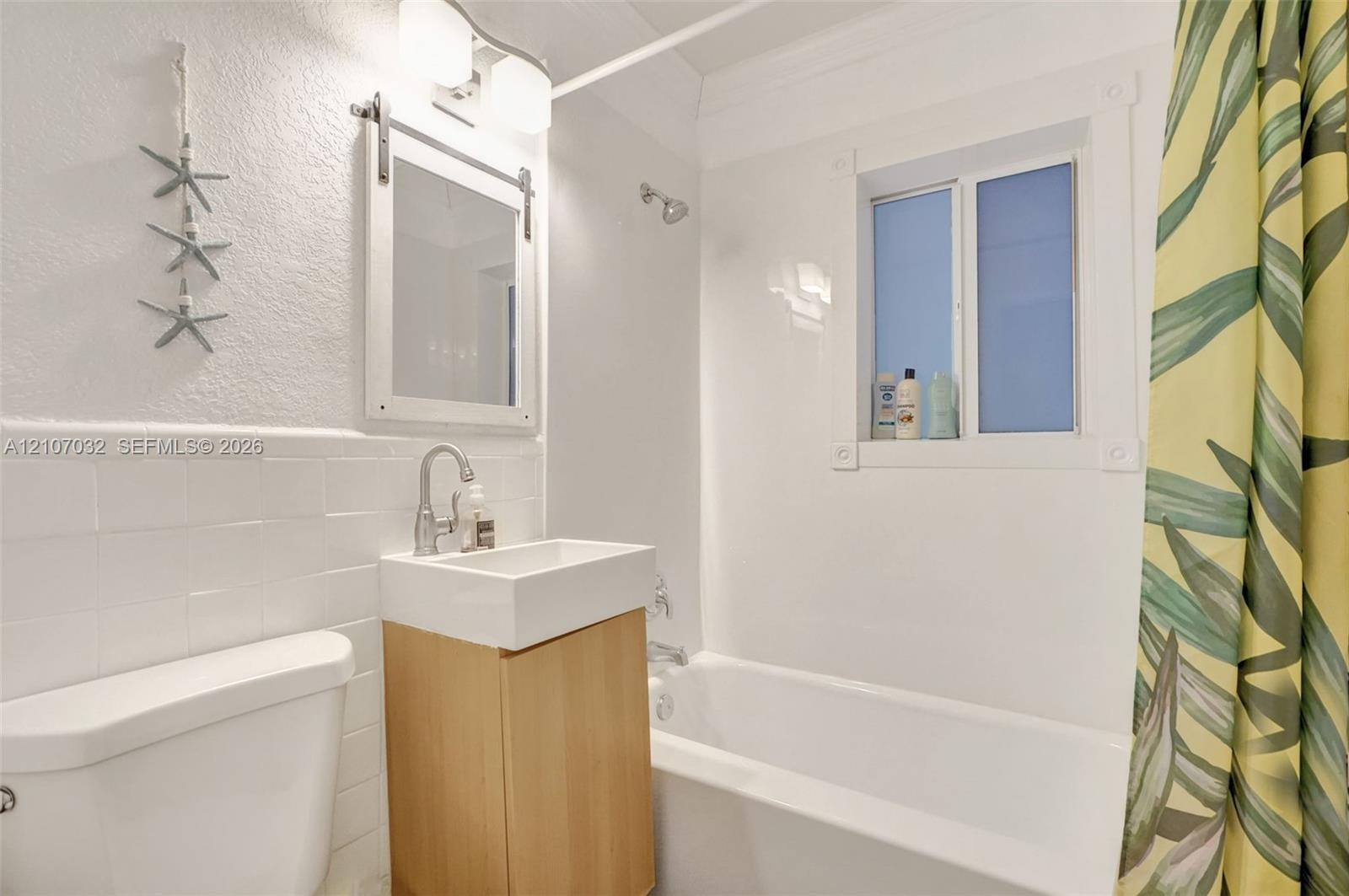 Bathroom featuring a wall-mounted vanity with a rectangular basin, subway tile wainscoting, sliding barn-door style mirror, and a built-in bathtub wit
