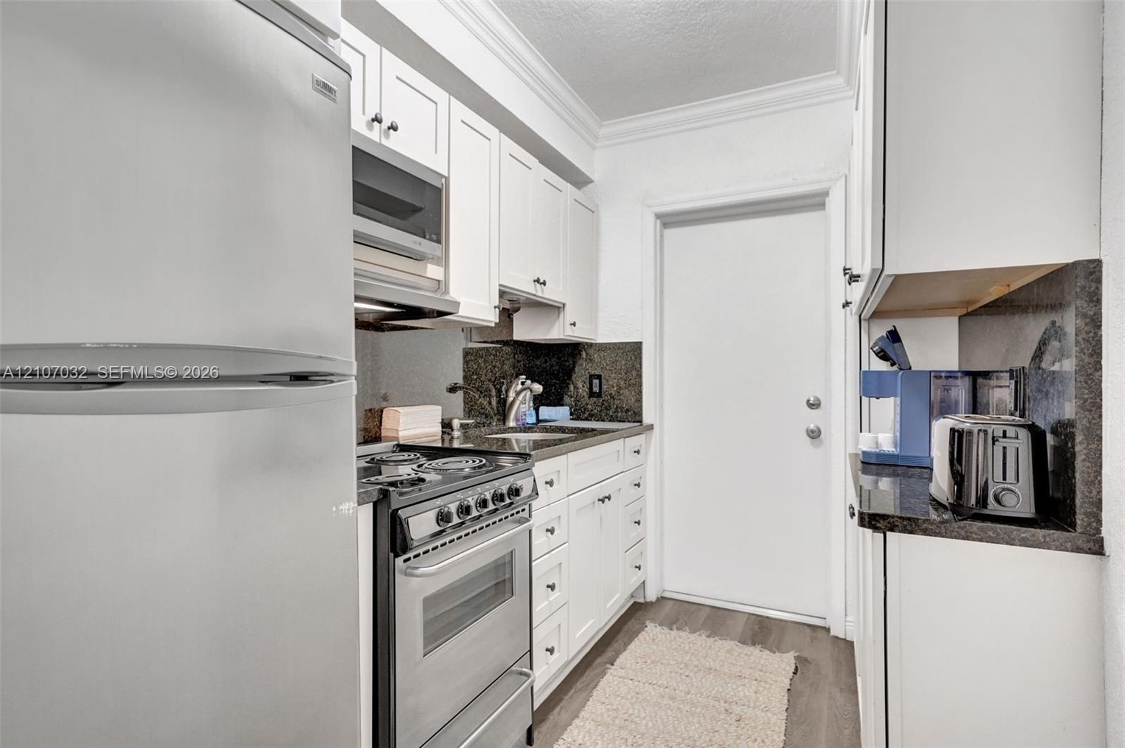 Kitchen featuring white shaker-style cabinetry, stainless steel appliances, dark stone-finish countertops, and wood-finish flooring