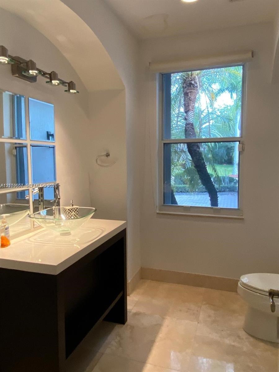 Vanity featuring a dark-toned base, white countertop, and clear glass vessel sink, complemented by a multi-pane mirror, wall-mounted lighting fixture,