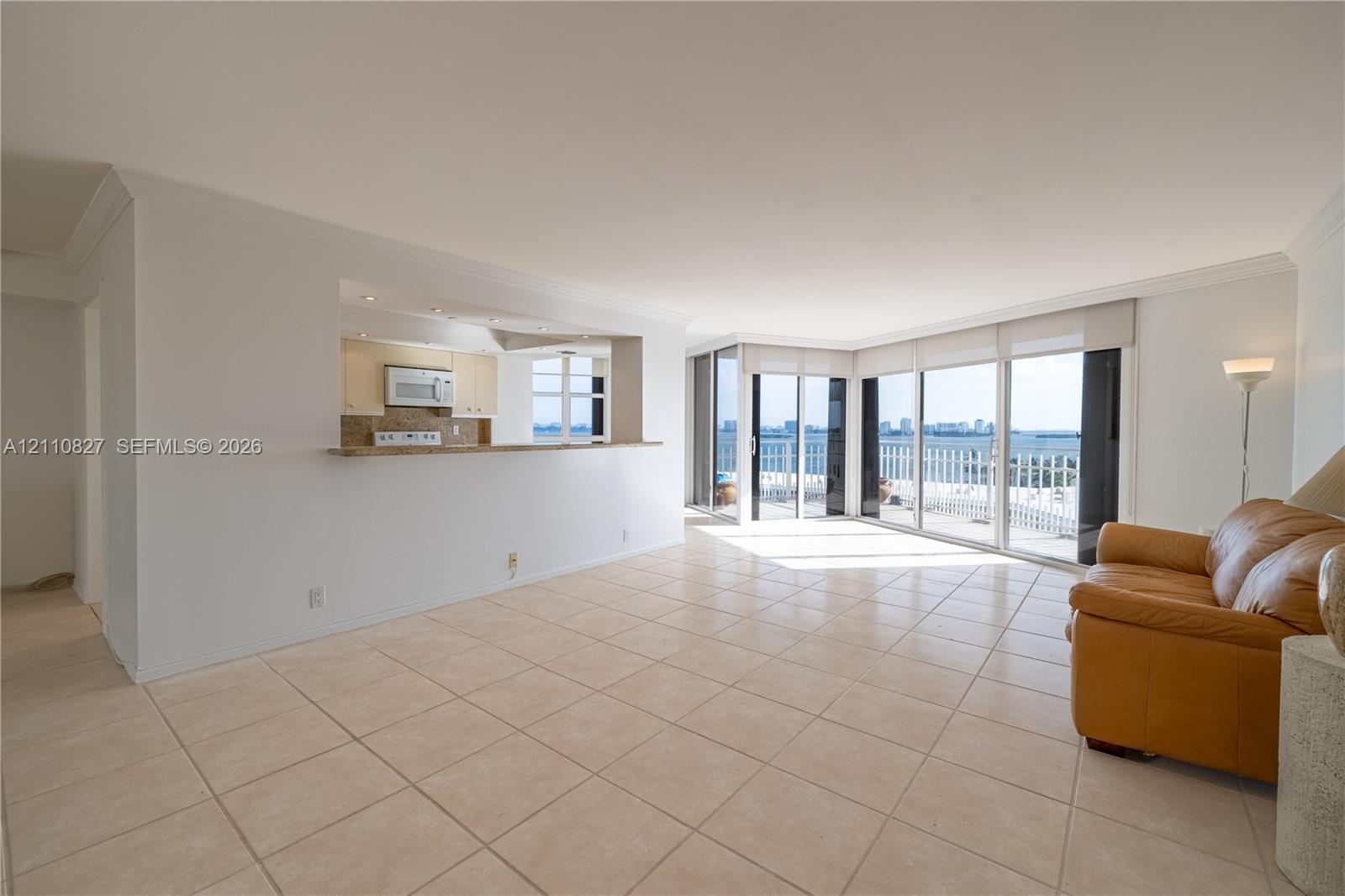 Open-concept area featuring light-toned ceramic tile flooring, a pass-through kitchen counter, and floor-to-ceiling glass sliding doors leading to an 