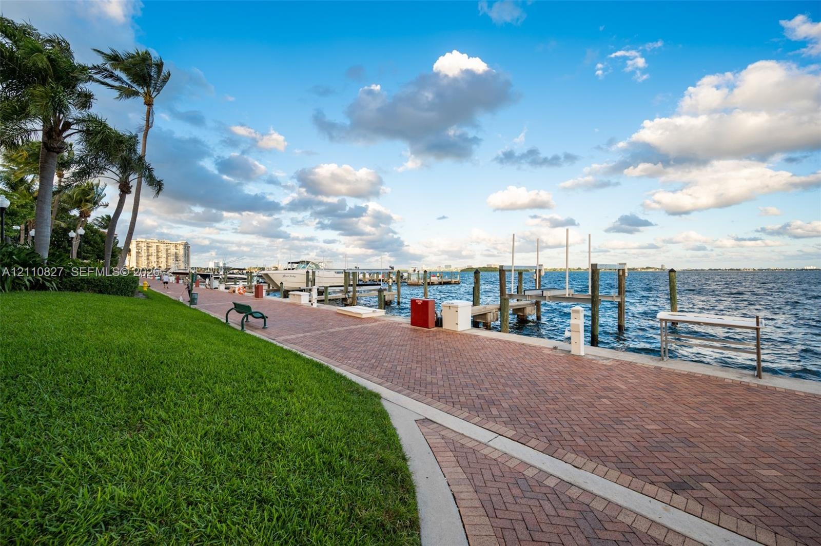 Waterfront promenade featuring a herringbone-patterned paver path, manicured lawn, and multiple deep-water boat slips