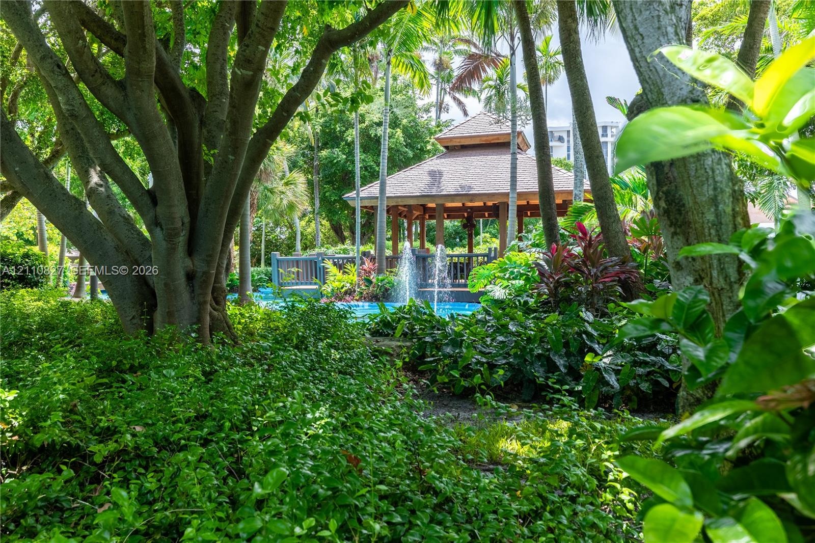 Outdoor grounds featuring a wooden gazebo, water fountain, mature palm trees, and lush landscaping