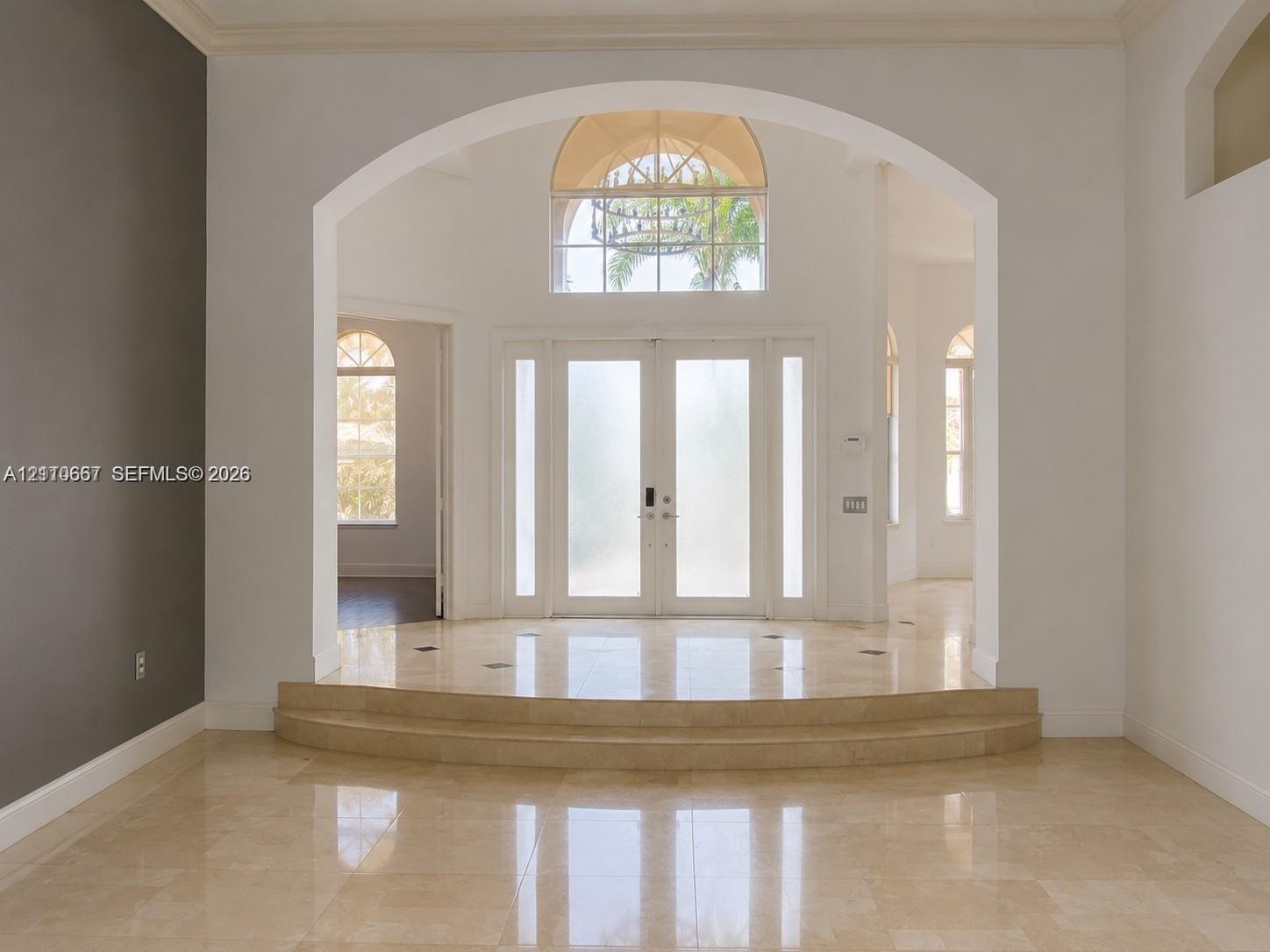 Entryway featuring stone tile flooring, a two-step raised landing, a vaulted arched entryway, double-door entry with sidelights, and an arched transom