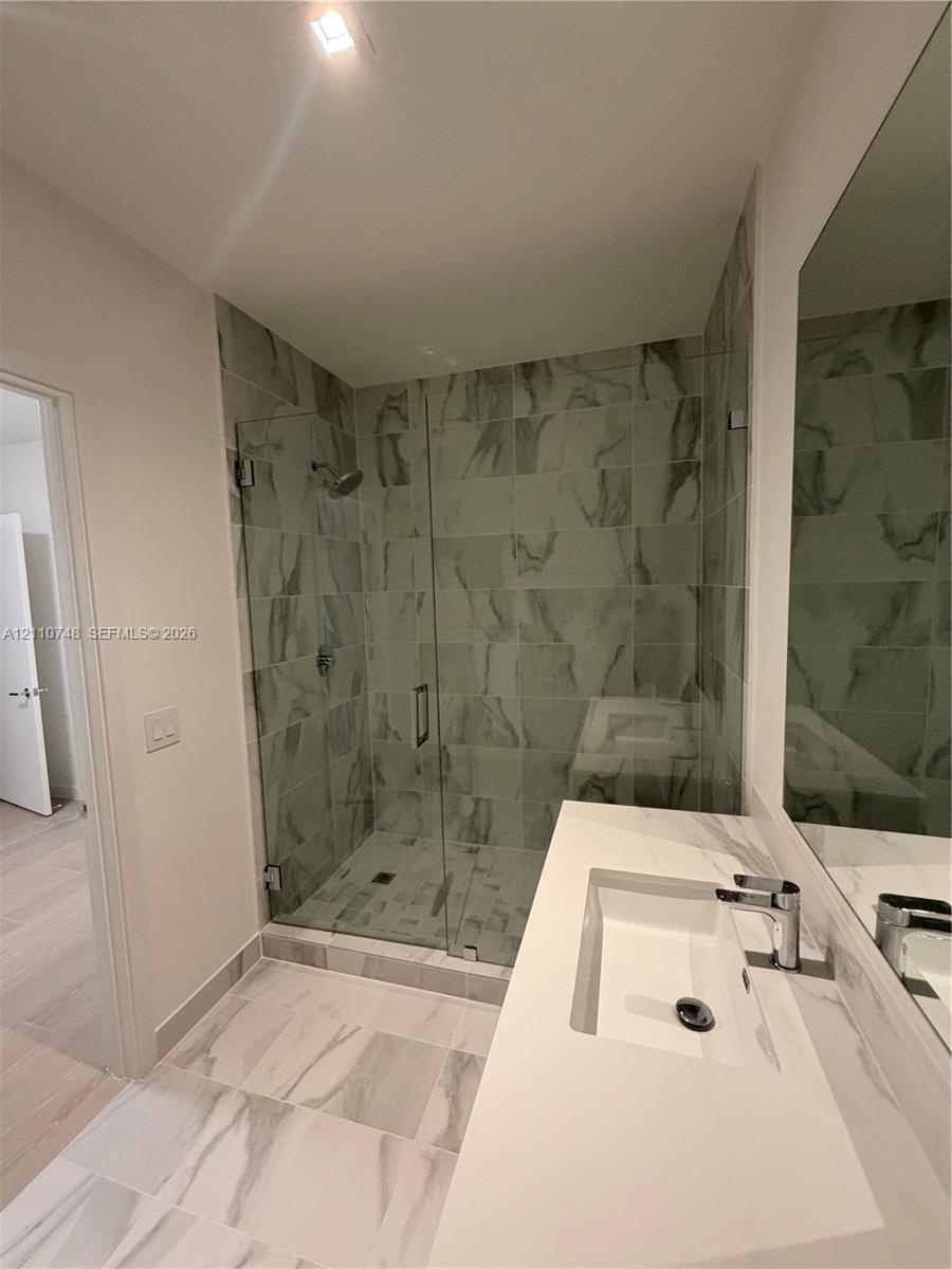 Walk-in shower with floor-to-ceiling tile, frameless glass enclosure, and wall-mounted shower head, paired with a white countertop vanity featuring an