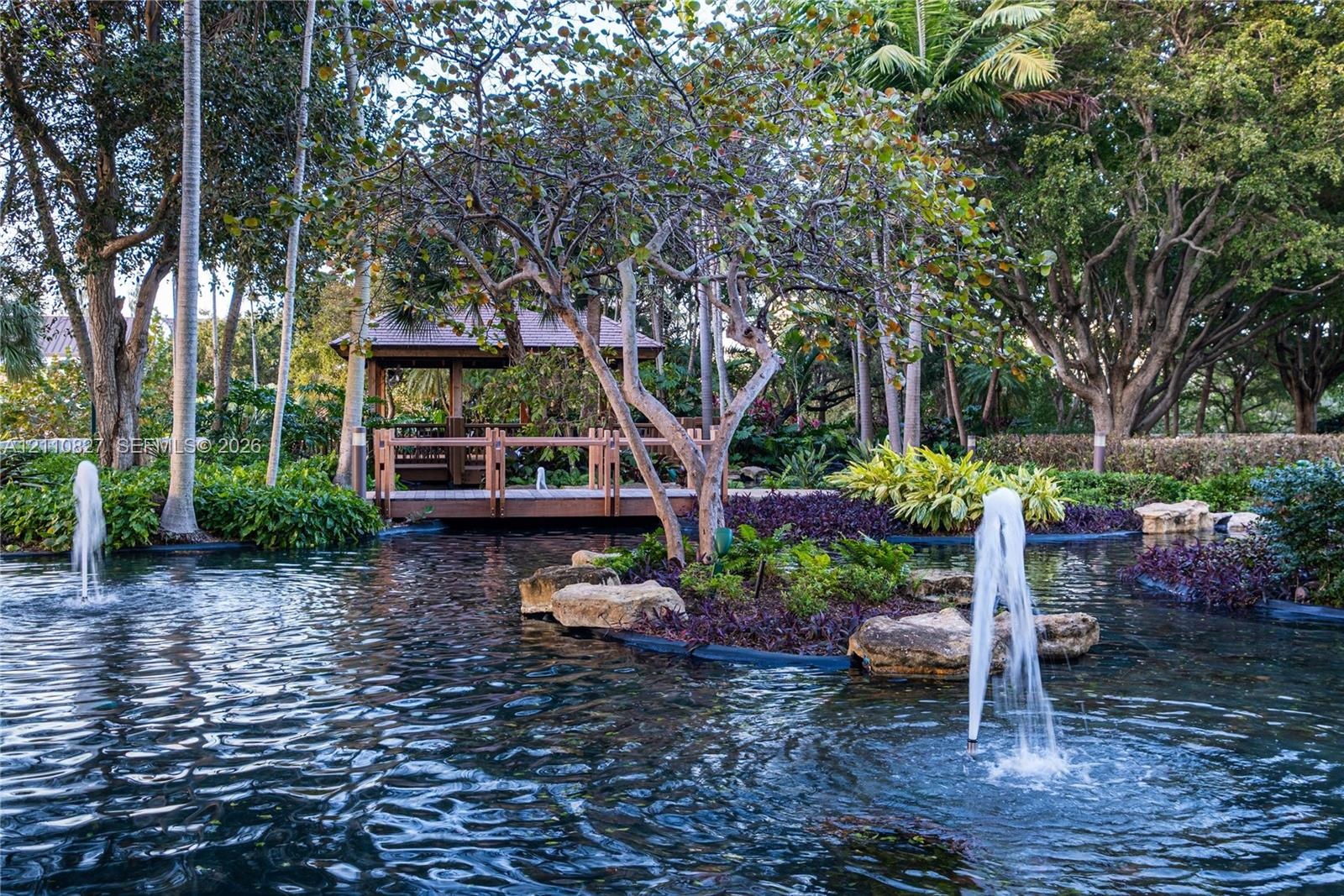 Water feature with dual fountains, pond, wood-framed gazebo, mature trees, and landscaped stone edging