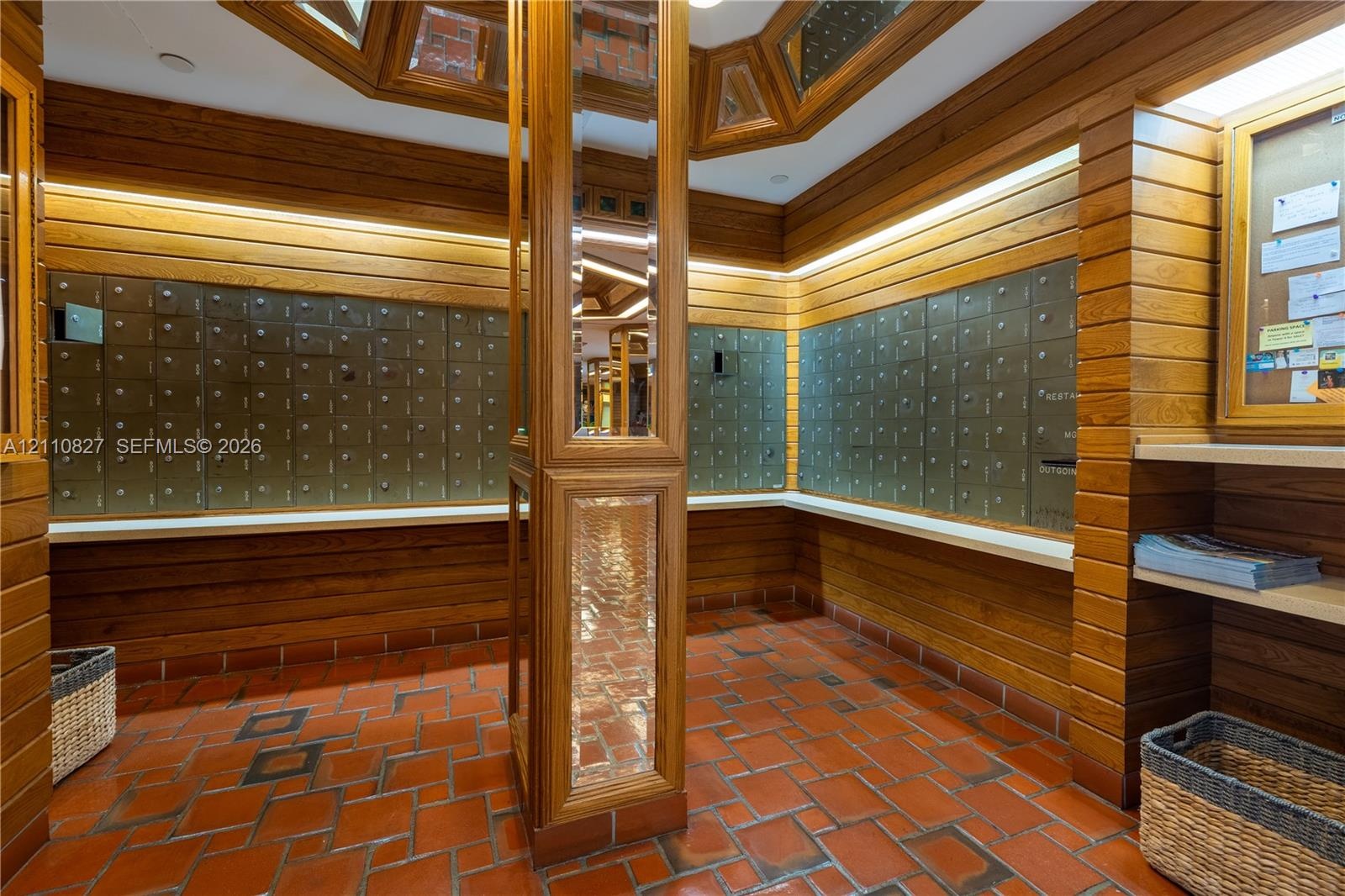 Mailroom area featuring horizontal wood paneling, terracotta tile flooring, built-in metal mailboxes, integrated task lighting, and a central column w