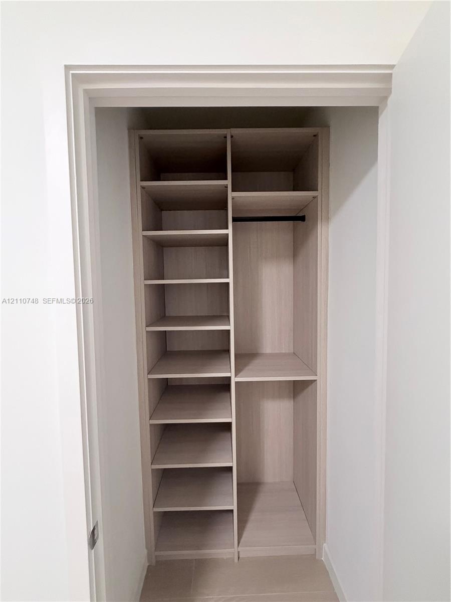 Built-in closet featuring light wood-finish shelving, multiple open storage compartments, and a horizontal hanging rod