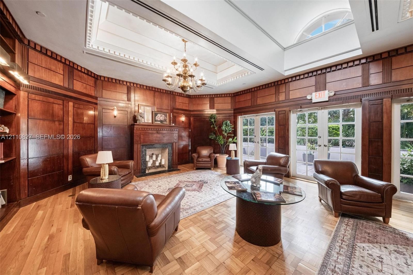Wood-paneled walls, coffered ceiling with integrated skylight, fireplace with masonry surround, parquet wood flooring, and double glass-paned doors