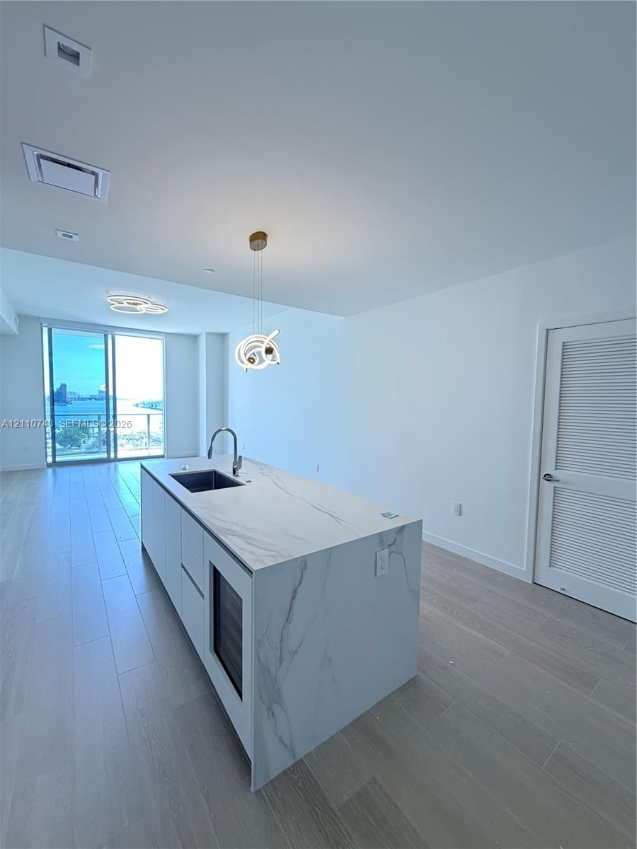Kitchen island with stone-finish waterfall countertop, undermount sink, built-in wine cooler, and high-arc faucet, complemented by wood-finish floorin