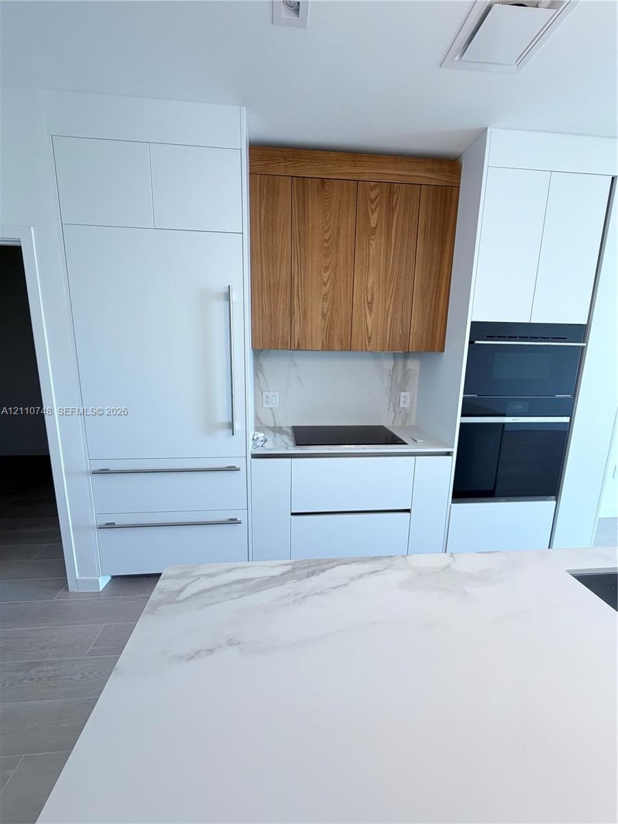 Custom cabinetry featuring contrasting wood-finish uppers and matte white base units, integrated refrigerator, built-in dual oven, stone-surface backs