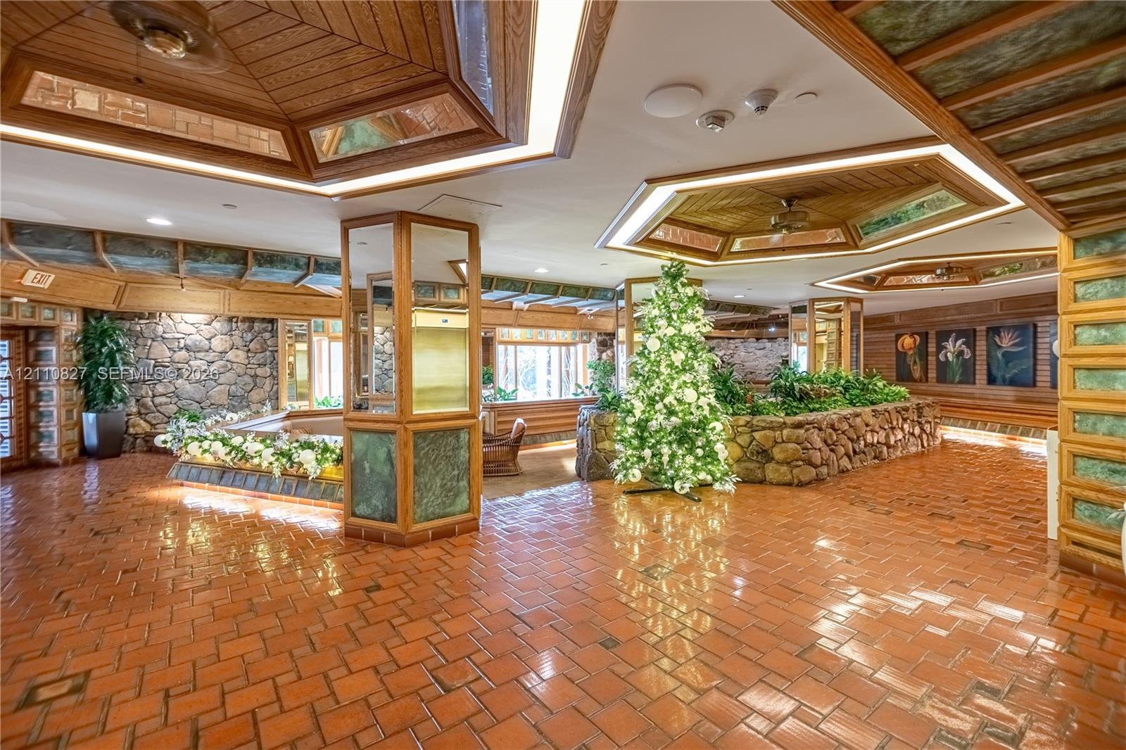Spacious interior featuring terra-cotta tile flooring, wood-paneled tray ceilings with integrated lighting, custom stone accent walls, and mirrored su
