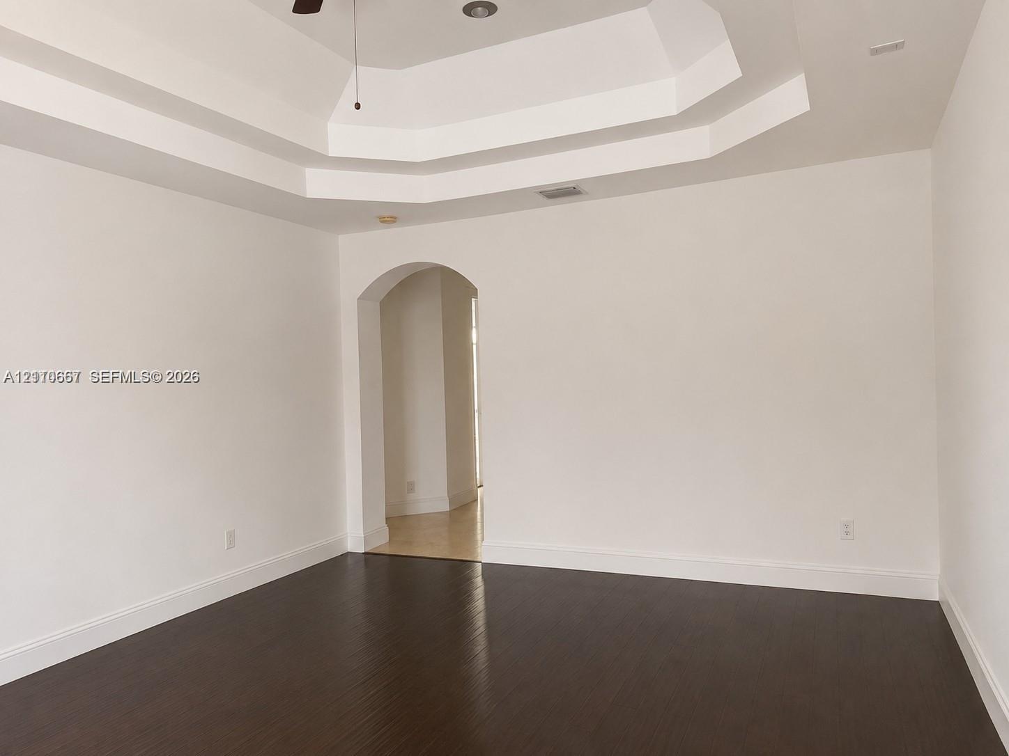 Room featuring a tray ceiling, arched entryway, and dark wood-finish flooring