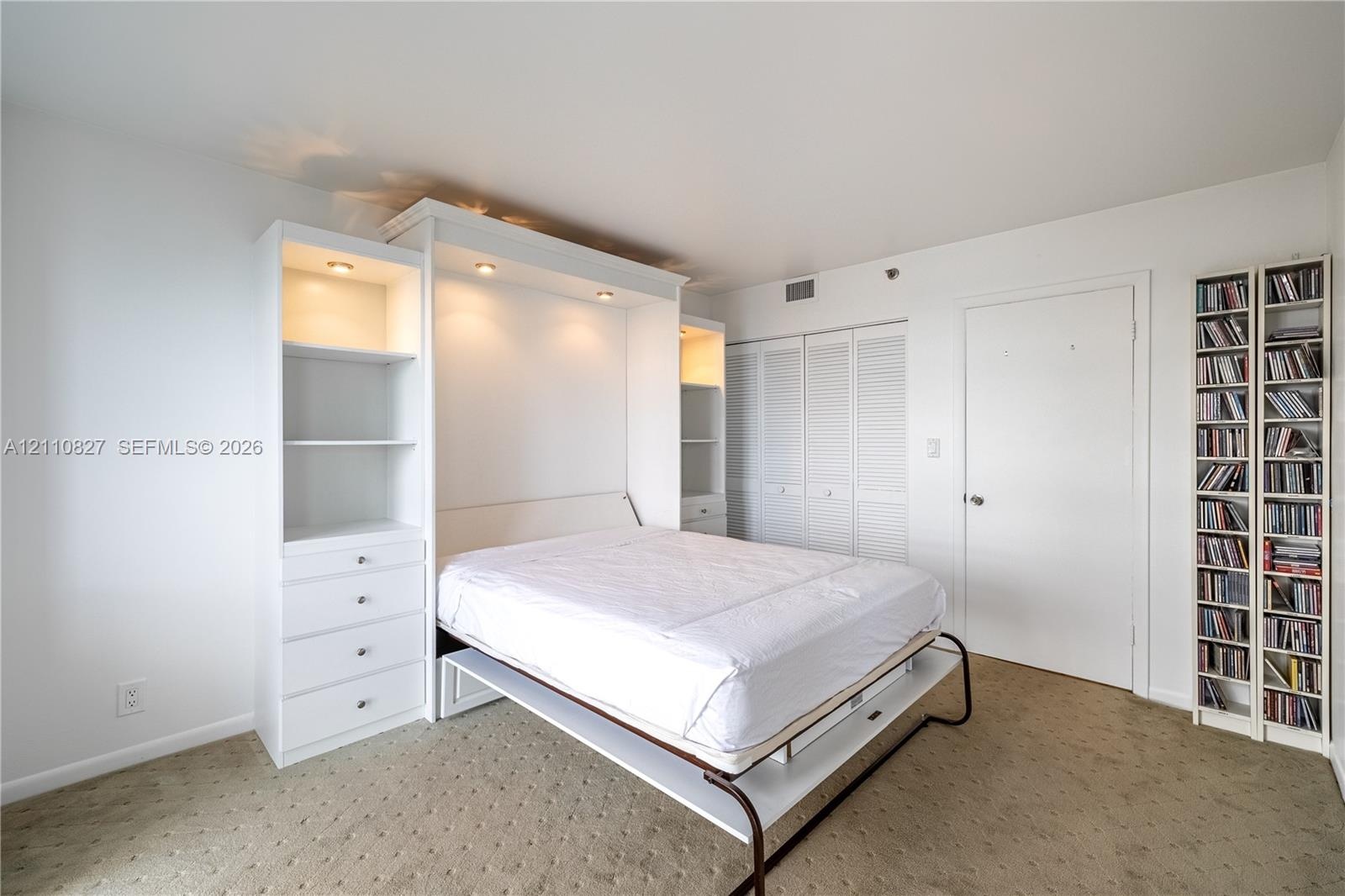 Custom white built-in cabinetry featuring integrated recessed lighting, four drawers, and shelving, paired with white louvered closet doors and carpet